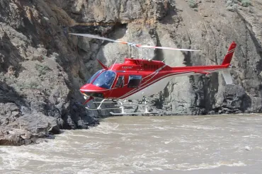 A helicopter flies low and fast through a steep river canyon