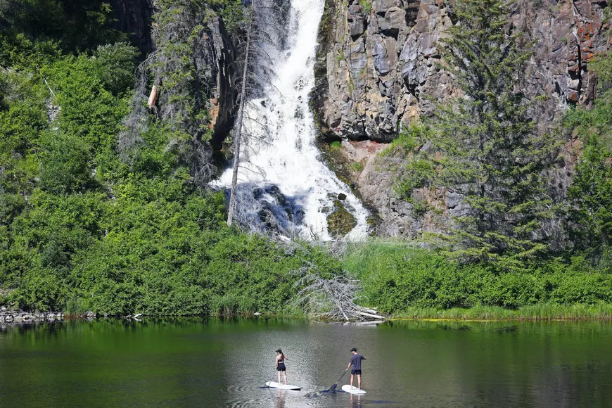 Paddle boarding under the waterfalls on the full day Crater Lake Adventure