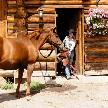 A woman learns to saddle a horse at the barn during a luxury horseback riding holiday at Siwash lake